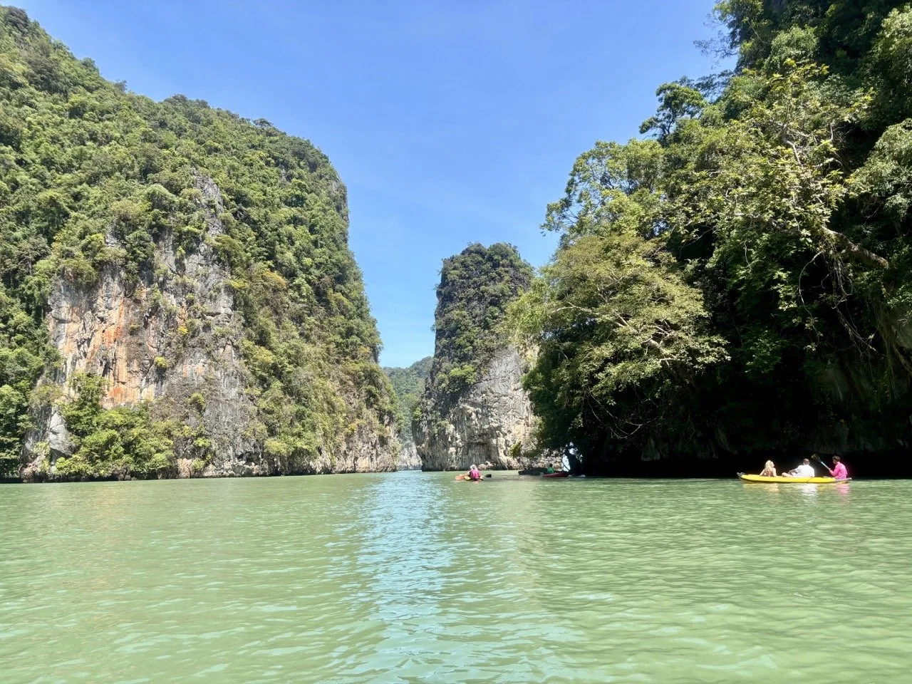 海上獨木舟進入攀牙灣石灰岩海蝕洞，洞口光影與湛藍海水形成充滿探險感的泰國旅遊畫面。