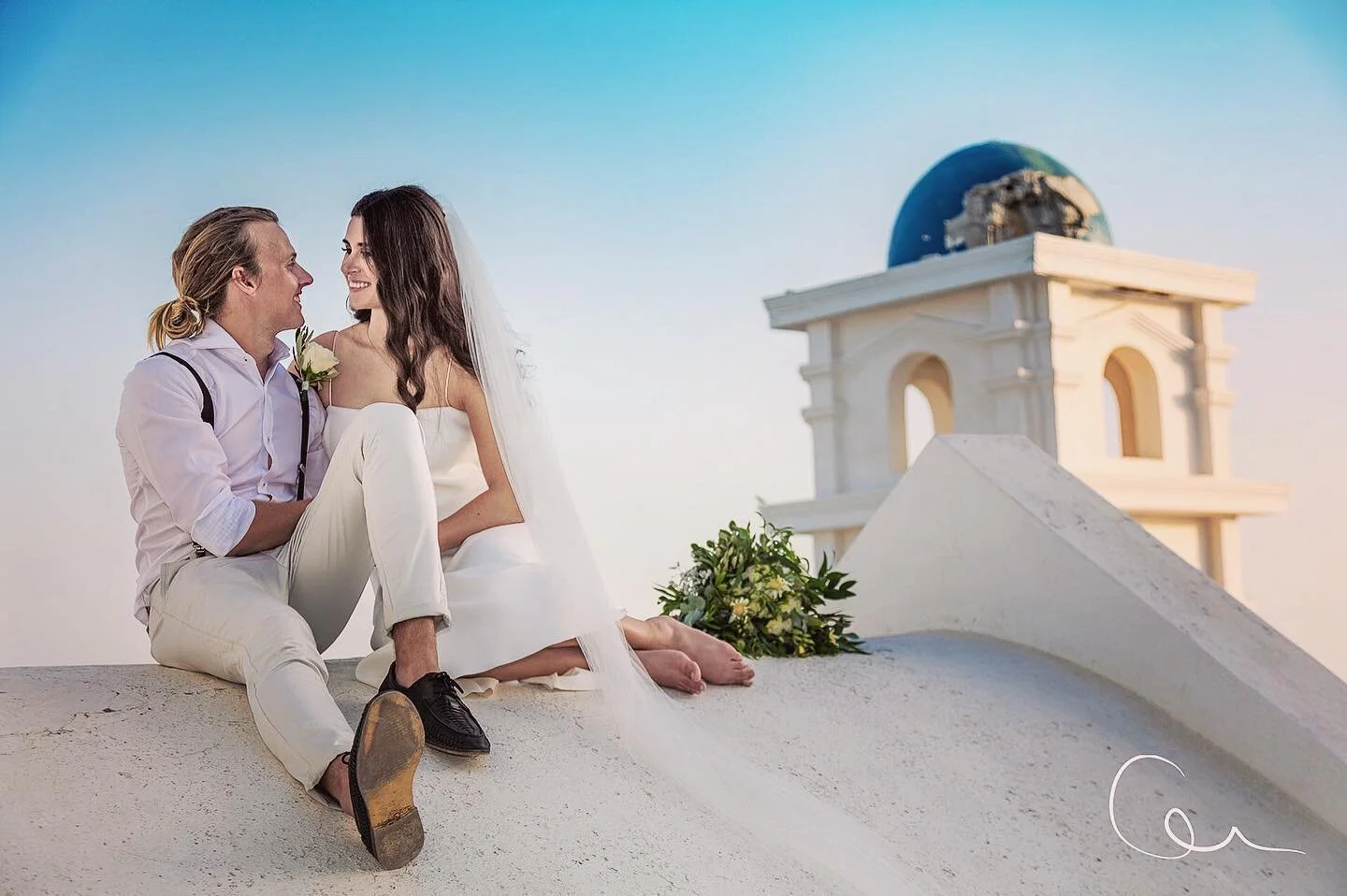 산토리니(Santorini) Oia 일몰 웨딩 촬영 모습: 블루돔 교회와 하얀 키클라데스 건축을 배경으로 골든아워에 촬영된 신랑신부의 로맨틱한 포트레이트. 허니문·웨딩 포토그래퍼 촬영, 선셋 스냅, 인게이지먼트·허니문 촬영에 최적화된 오이아( Oia ) 대표 포토스팟과 카르데라 전망을 보여주는 고해상 이미지.
