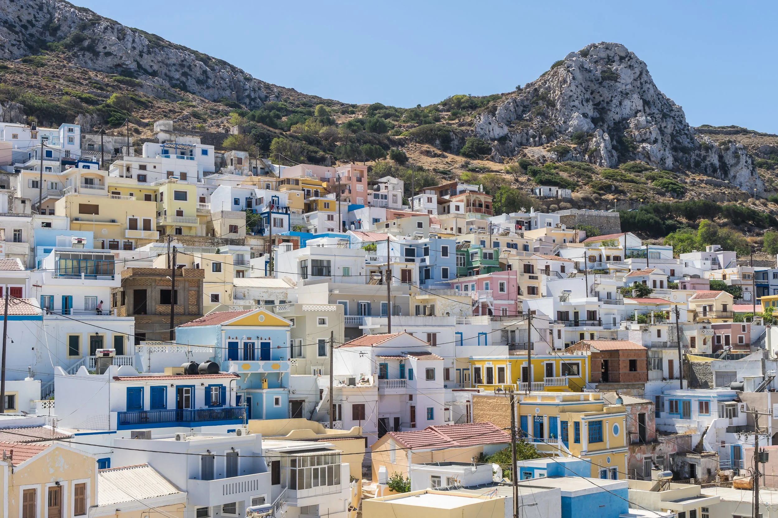 カルパトス島（Karpathos）旅行ガイド用画像：伝統的な白い家屋と狭い石畳の路地、透き通るエーゲ海に面した絶景ビーチを捉えたビジュアル。ゴールデンアワーの撮影スポット、地元の村歩きやグルメ、フェリーアクセス情報を連想させる典型的なカーペソス（Karpathos）のフォトスポット画像で、インスタ映えする旅写真やビーチリゾートの参考に最適です。