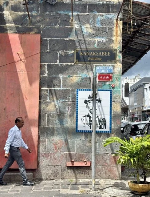 路易斯港中央市場巷弄與攤販近拍，遊客品嚐 Dholl Puri 與 Alouda，展現模里西斯在地美食文化與市場漫遊景象