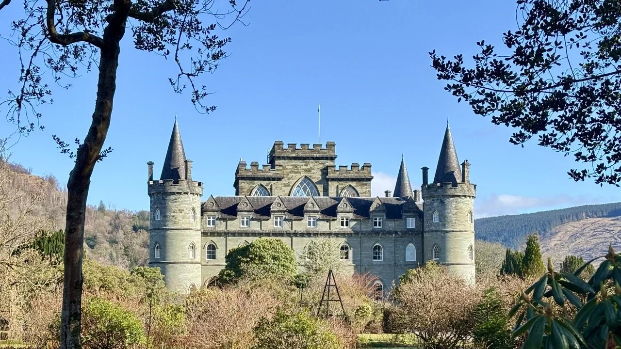 史塔克城堡 Castle Stalker 與遠方蘇格蘭山脈構成壯麗風景，古堡位於湖面之中，展現蘇格蘭高地歷史建築與自然景觀結合的魅力。Castle Stalker and the surrounding Scottish mountains create a dramatic landscape of historic architecture and natural beauty.