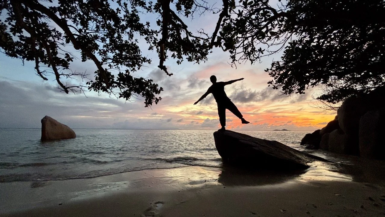 塞席爾 Anse Lazio 海灘日落景色，夕陽照亮海面與花崗岩岩石，營造寧靜浪漫的普拉蘭島海岸風光。