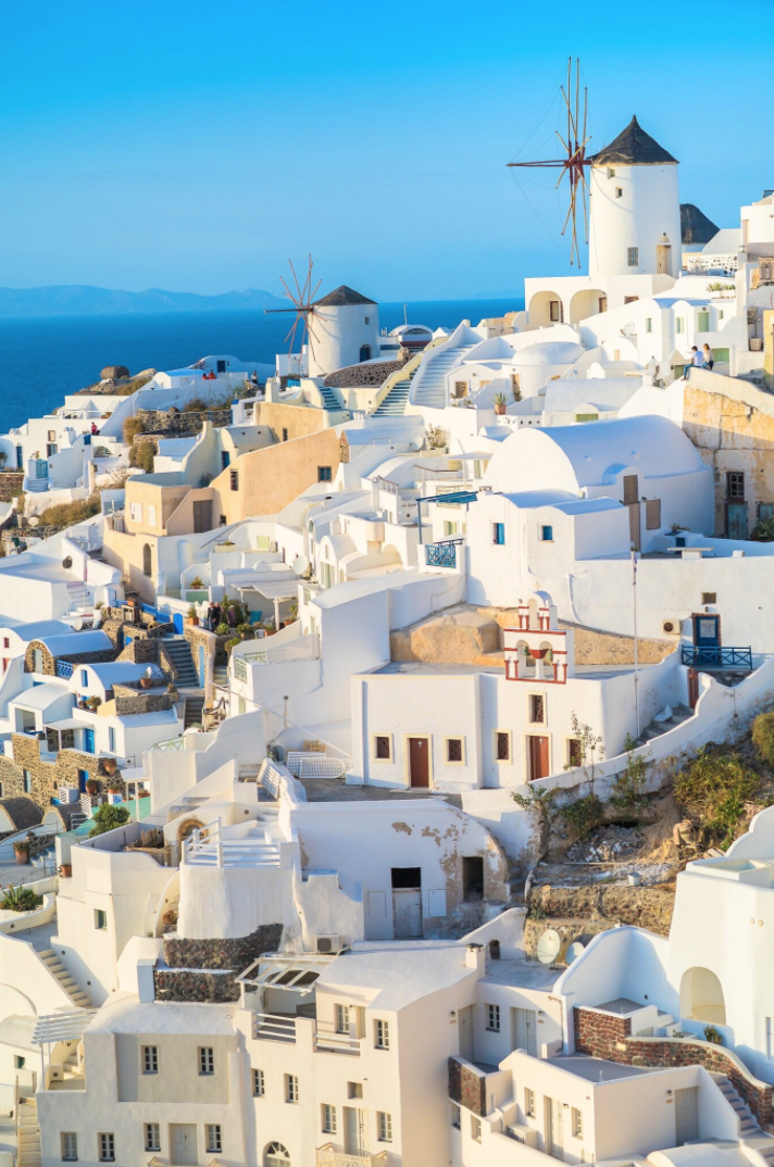 Santorini Oia caldera sunset panorama with couple posing on whitewashed terraces, golden hour lighting and professional composition for wedding photography.