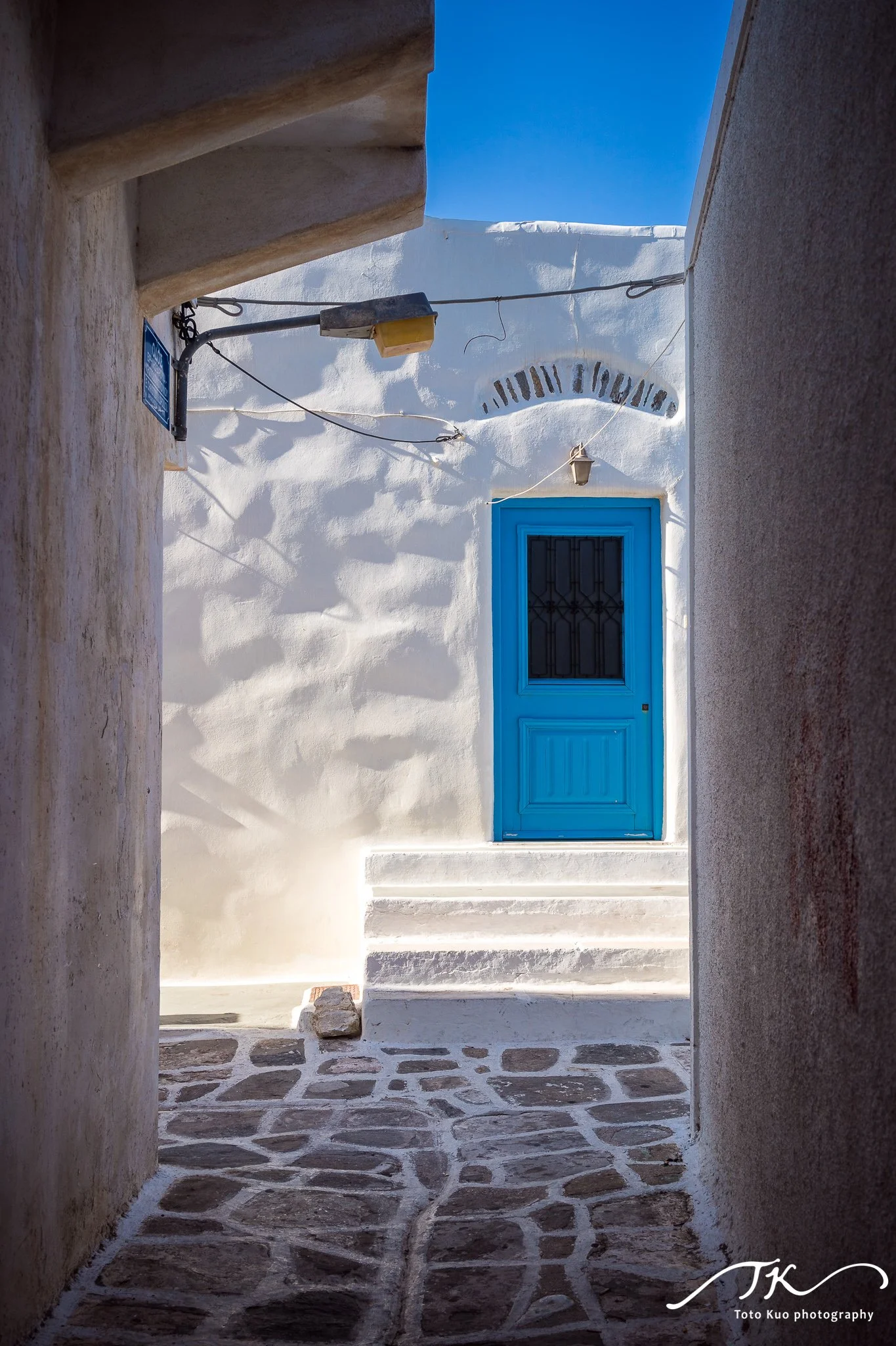 Paros 巷弄街拍：白牆、藍窗與市集生活，旅遊全攻略中人文攝影篇章的重點範例。 / Paros street photography charm: white walls, blue shutters and market life—highlighted in the travel guide’s cultural photography section.