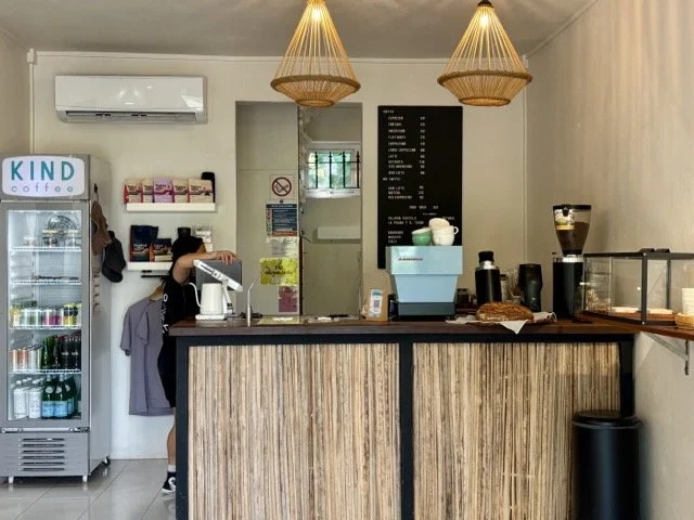 Kind Coffee 靠窗座位與拉花拿鐵近拍，窗外自然光映照桌上酸種麵包與鹹派，適合模里西斯早餐、Brunch 與咖啡師手沖教學相關搜尋