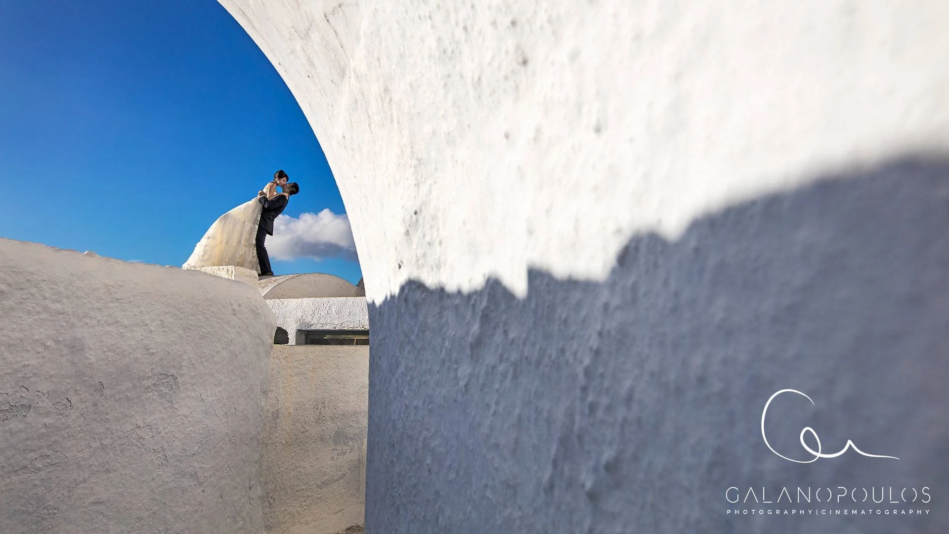 Oia 隱藏巷弄婚紗場景：白牆拱門與花盆前景，低調浪漫的私房拍攝地點；Oia hidden alley wedding scene — whitewashed arches and potted foregrounds for understated romantic shoots.