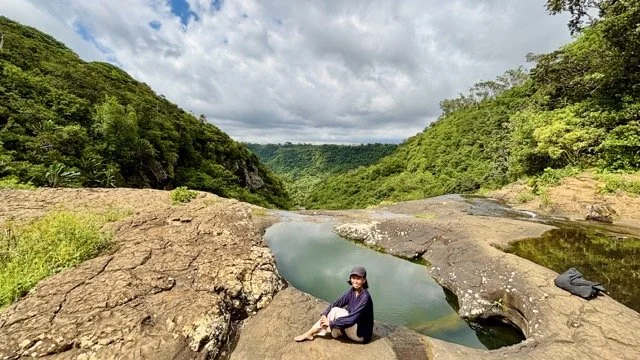 七瀑布下方天然清澈泳池特寫，遊客在池邊休憩與野泳的場景，示範模里西斯生態旅遊與夏日消暑體驗。 Close‑up of natural clear pools beneath Seven Waterfalls with visitors resting and wild swimming—illustrating Mauritius eco‑tourism and summer refreshment.