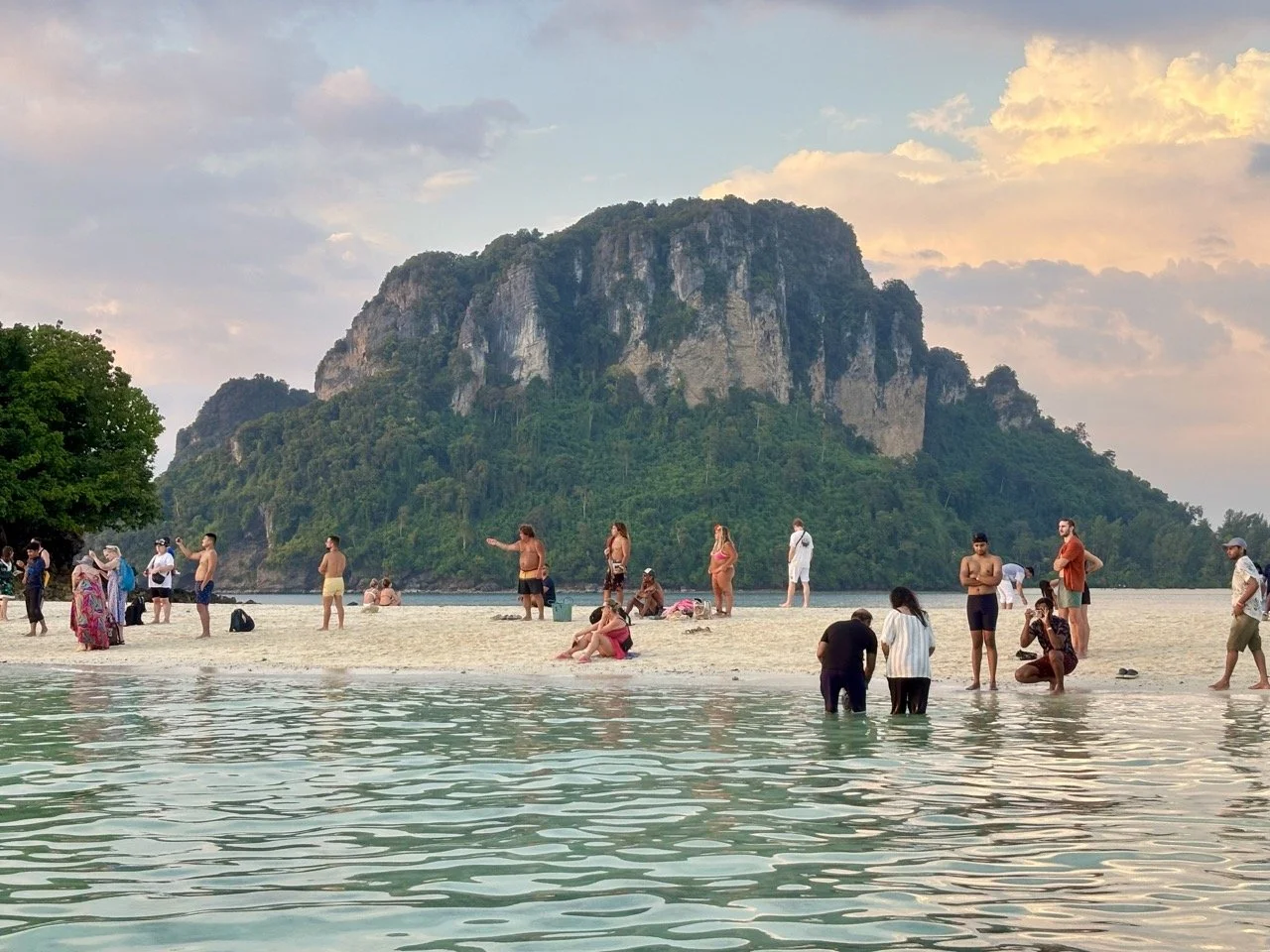 甲米奧南海灘日落景色，夕陽映照海面與遠方山巒，是泰國 Krabi 海邊散步及欣賞黃昏風景的熱門地點。 Sunset at Ao Nang Beach in Krabi, with warm evening light reflecting across the sea and distant mountains.