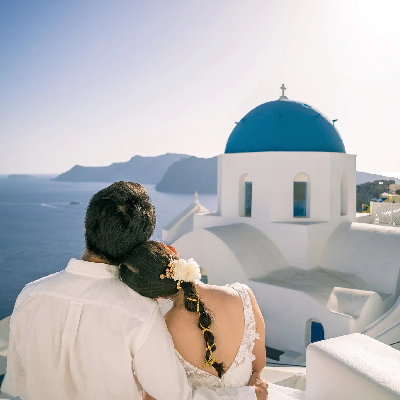 藍頂教堂空拍總覽（合規 drone 拍攝）：俯瞰 Oia 的藍白建築群與愛琴海，Santorini aerial wedding shot（需許可）；Blue domes aerial overview (regulated drone) — panoramic view of Oia’s blue‑white rooftops and Aegean Sea for Santorini aerial wedding shots (permits required).