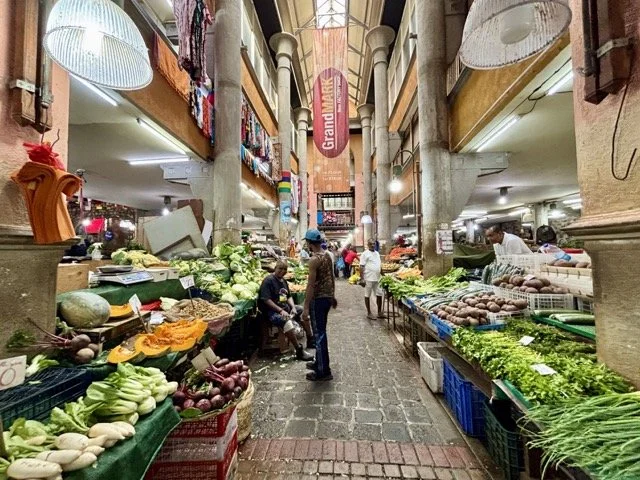 Port Louis 市場巷弄小吃攤連拍，遊客邊走邊吃在地小吃體驗，文化深度旅遊實例。 Series of snack stalls in Port Louis market alleys with tourists tasting street food while walking—a deep cultural travel example.