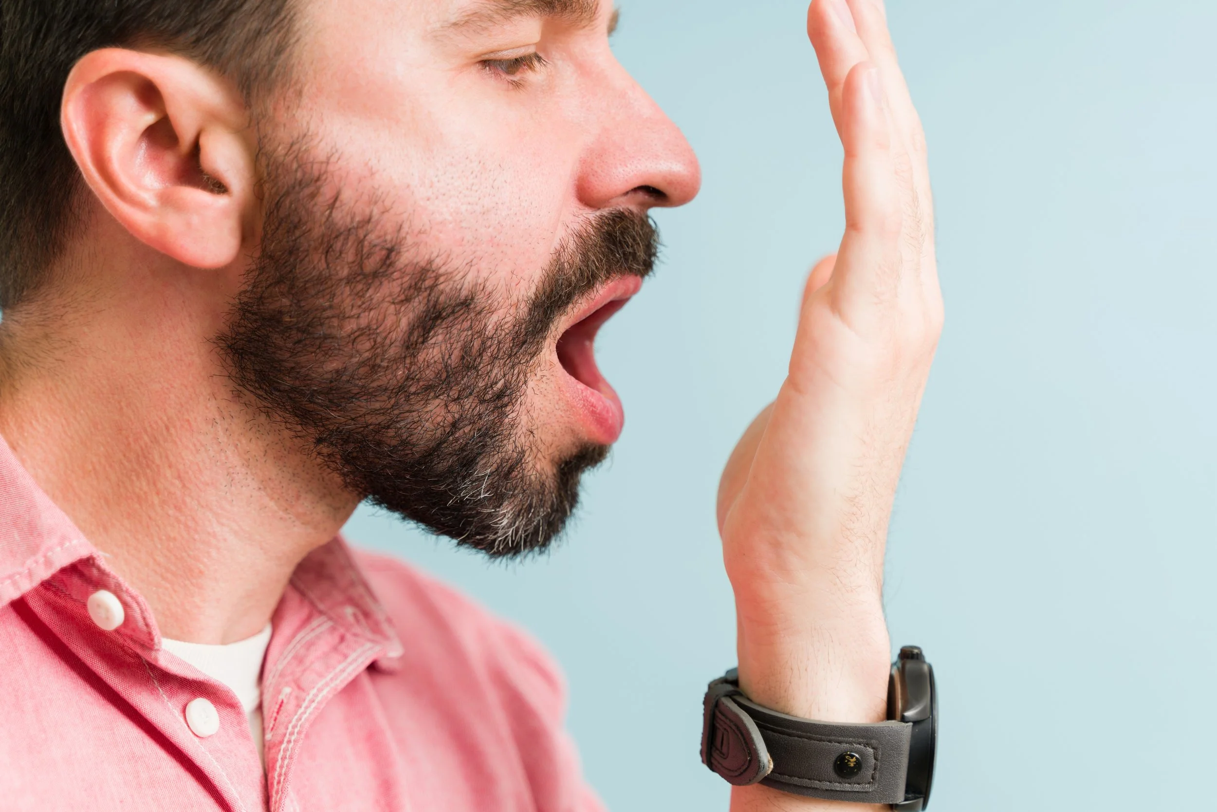 Man holding up hand and breathing into it to check how breath smells