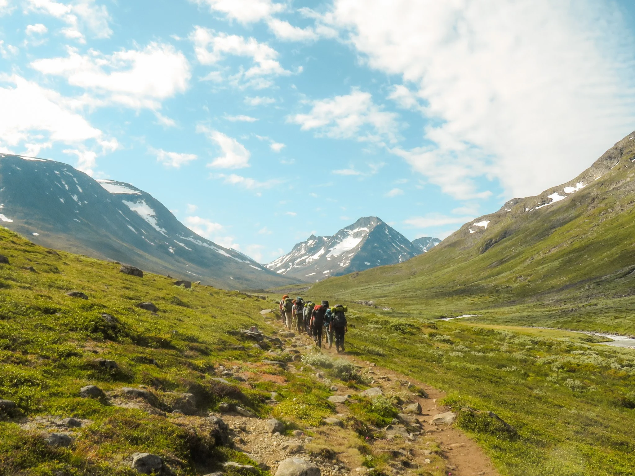 Travelers walking a remote volcanic trail toward snow-capped mountains