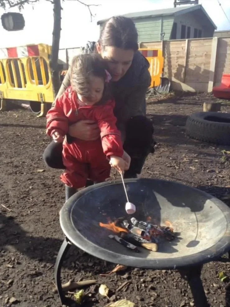 A woman and a young girl roasting marshmallows over a small outdoor fire pit.