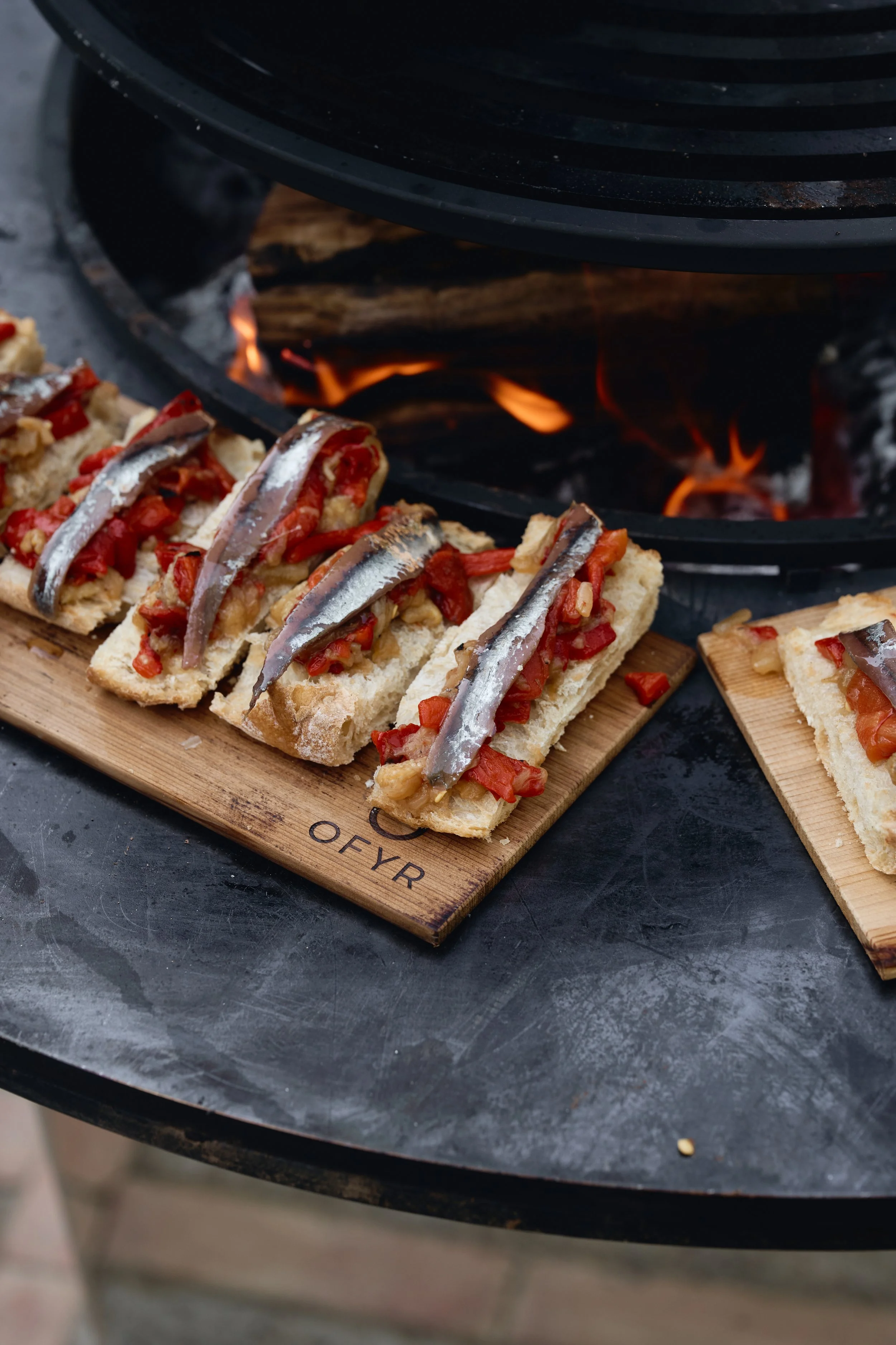 Open vuur met gerookte makreel pizza's op houten plank op een zwarte tafel.