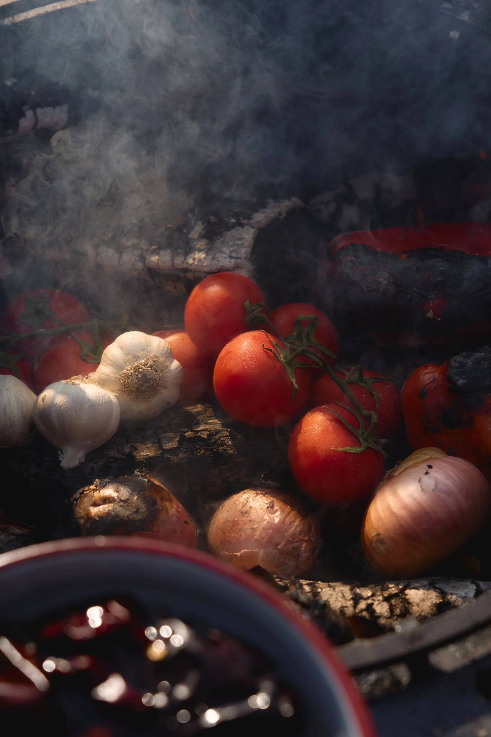 Tomaten, knoflook en uien in de rook van het open vuur bij Vegetables on Fire