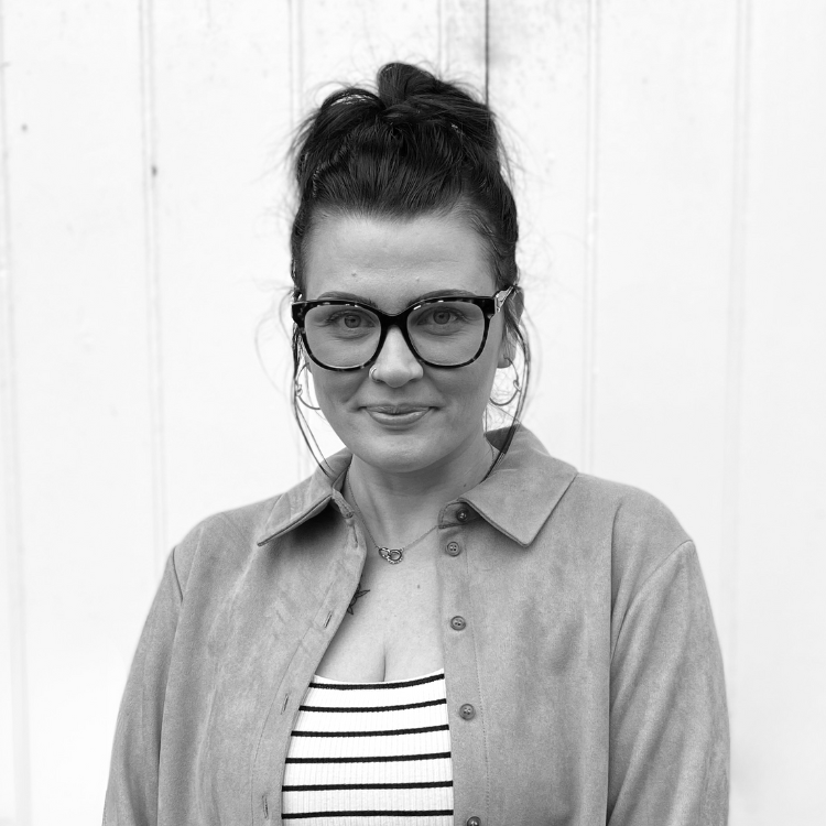 Black and white photo of a woman with shoulder-length dark hair and a nose piercing, smiling