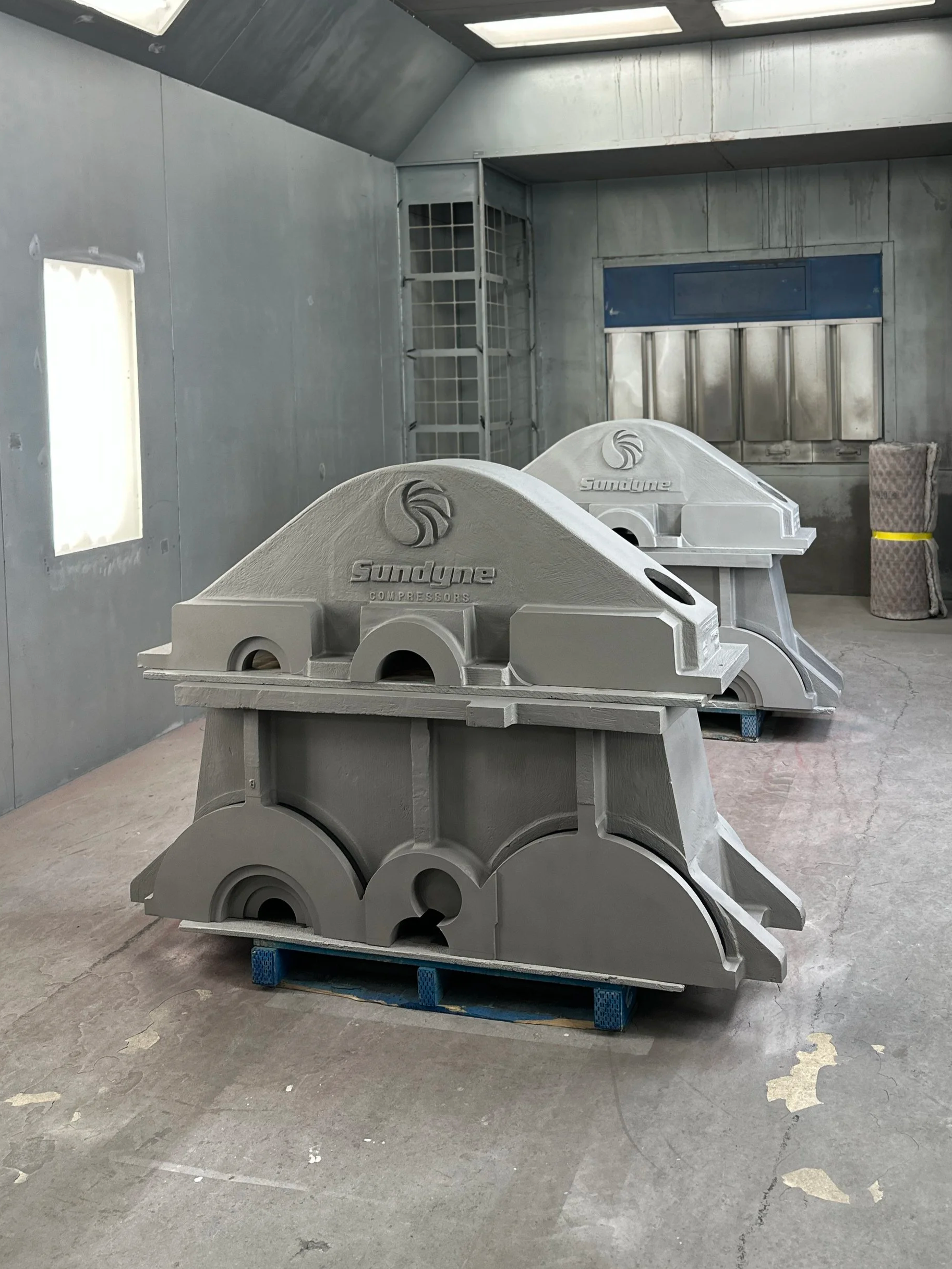 Steel industrial gearboxes labeled 'Sundyne Compressors' inside an industrial paint booth