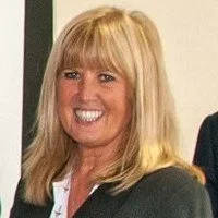 Woman with blonde hair smiling, wearing a dark blazer.