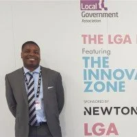 Man in suit and tie standing next to a banner with text about the LGA and innovation zone.