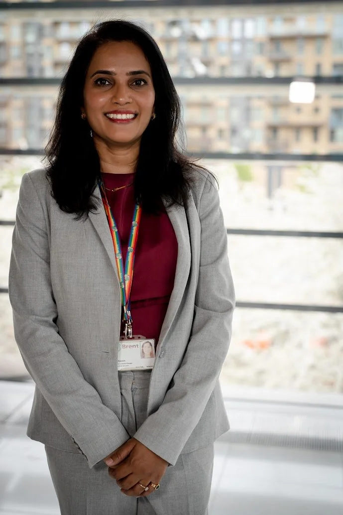 A smiling woman in a gray business suit standing indoors with a cityscape in the background.