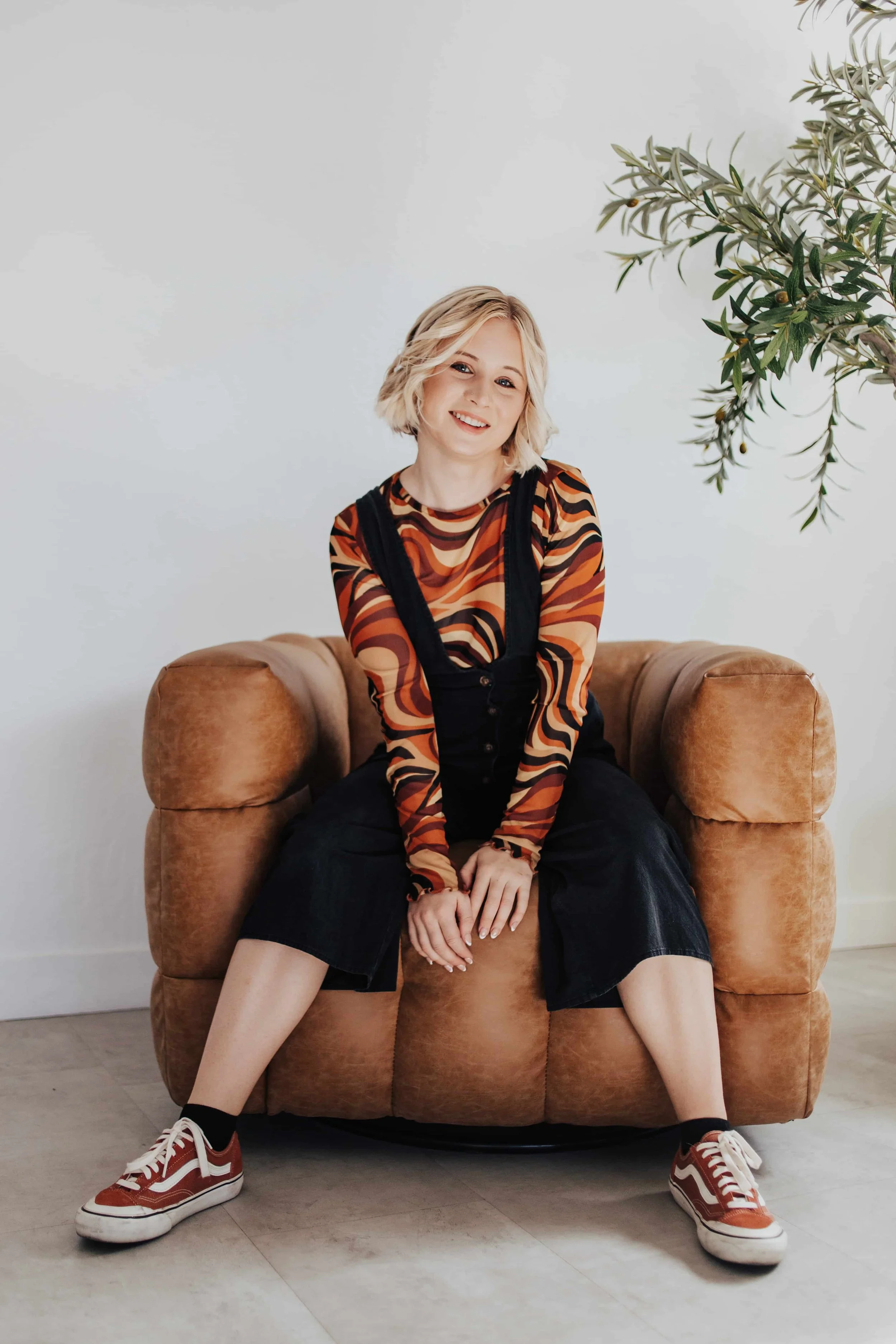 A photographer sits for a brand photo in a neutral colored chair.
