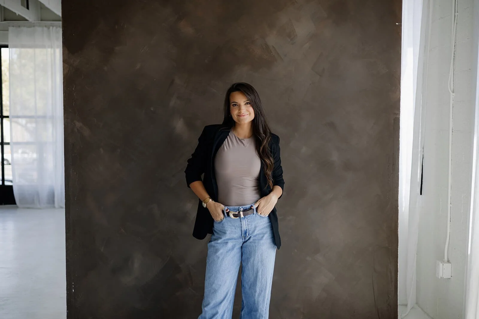 A professional young photographer poses in front of a wall the color of her brand palette.