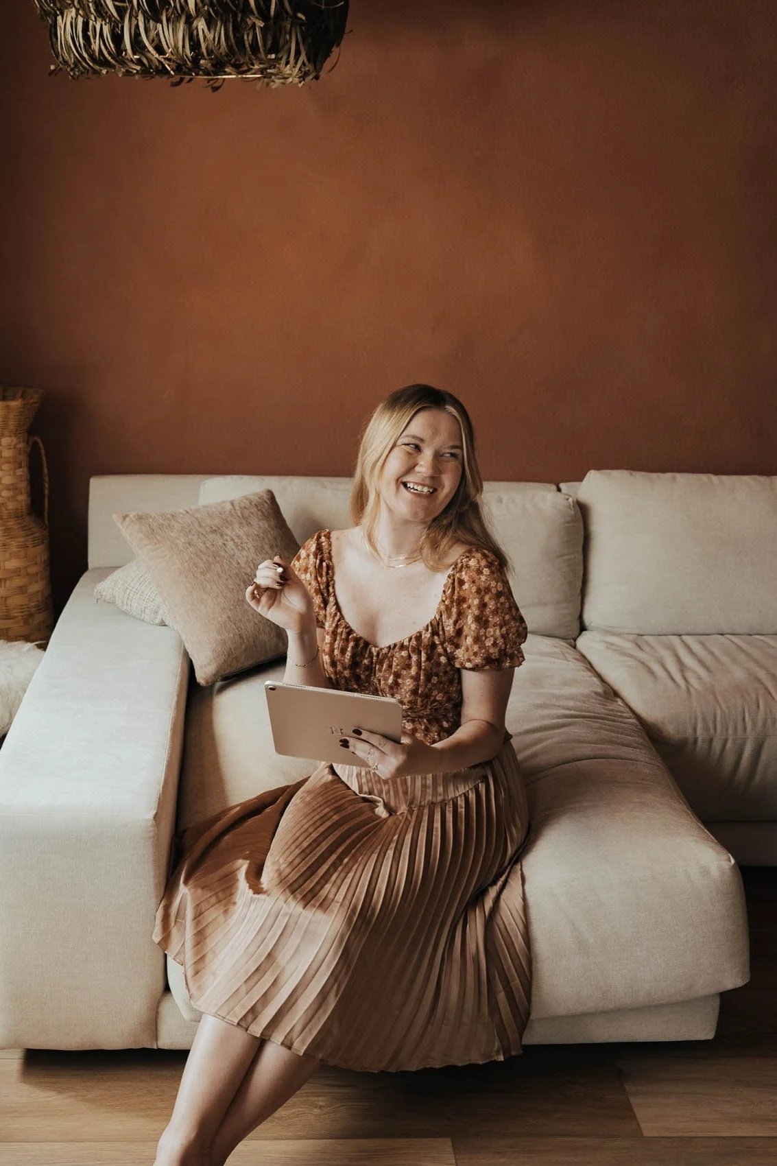 Aliya Mooney is the founder and sole creative of Hearthstone Creative, a boutique branding agency focused on providing strategy-forward brand solutions for established small businesses. Aliya is sitting on a couch in a well-lit room holding an iPad.