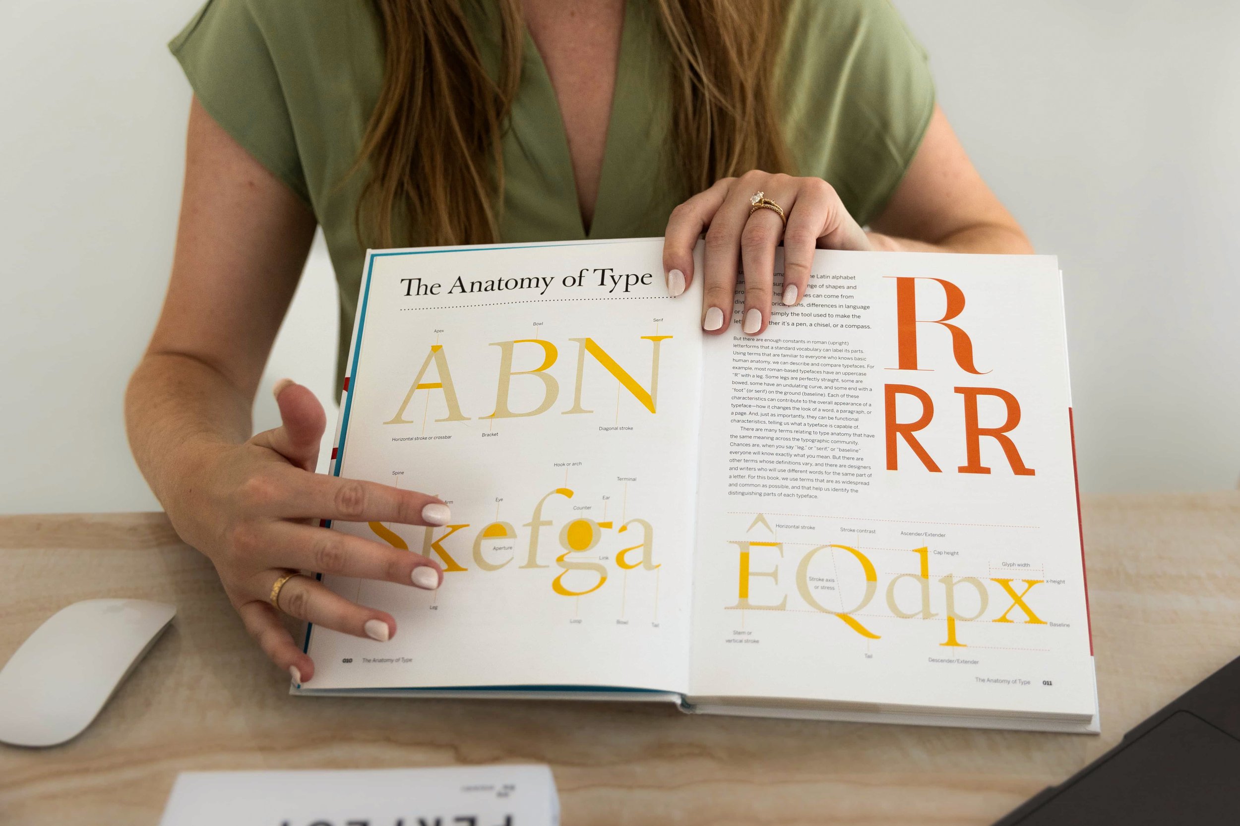 A young woman holding a book that displays anatomy of typefaces and pointing to a page.