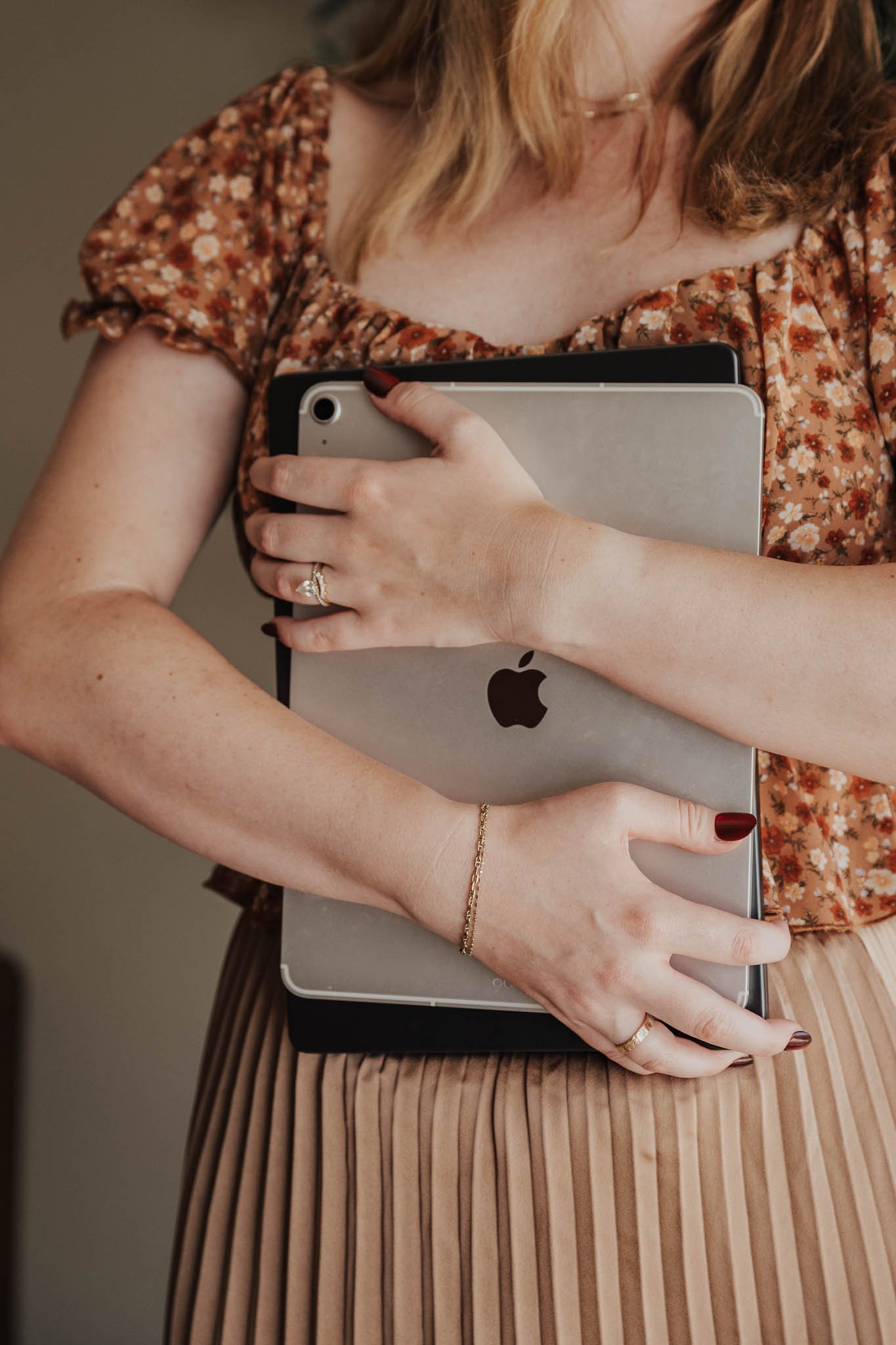 A woman holds her laptop and iPad to her chest and looks out the window.