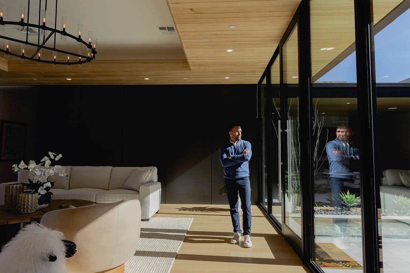 A luxury real estate agent posing in a high-end living room, with arms crossed.