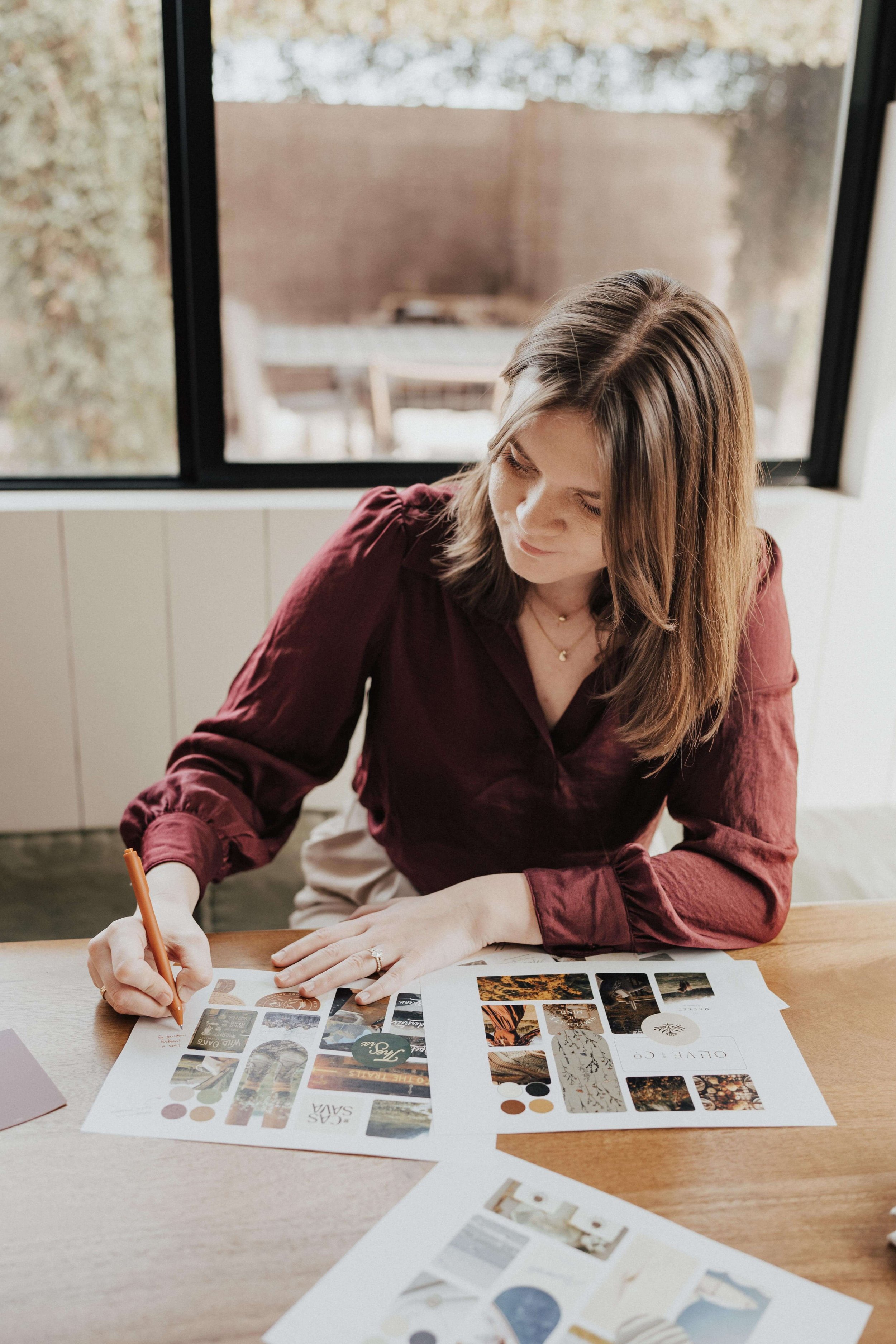 A brand designer sits at a kitchen table, writing notes on mood boards for her branding clients.