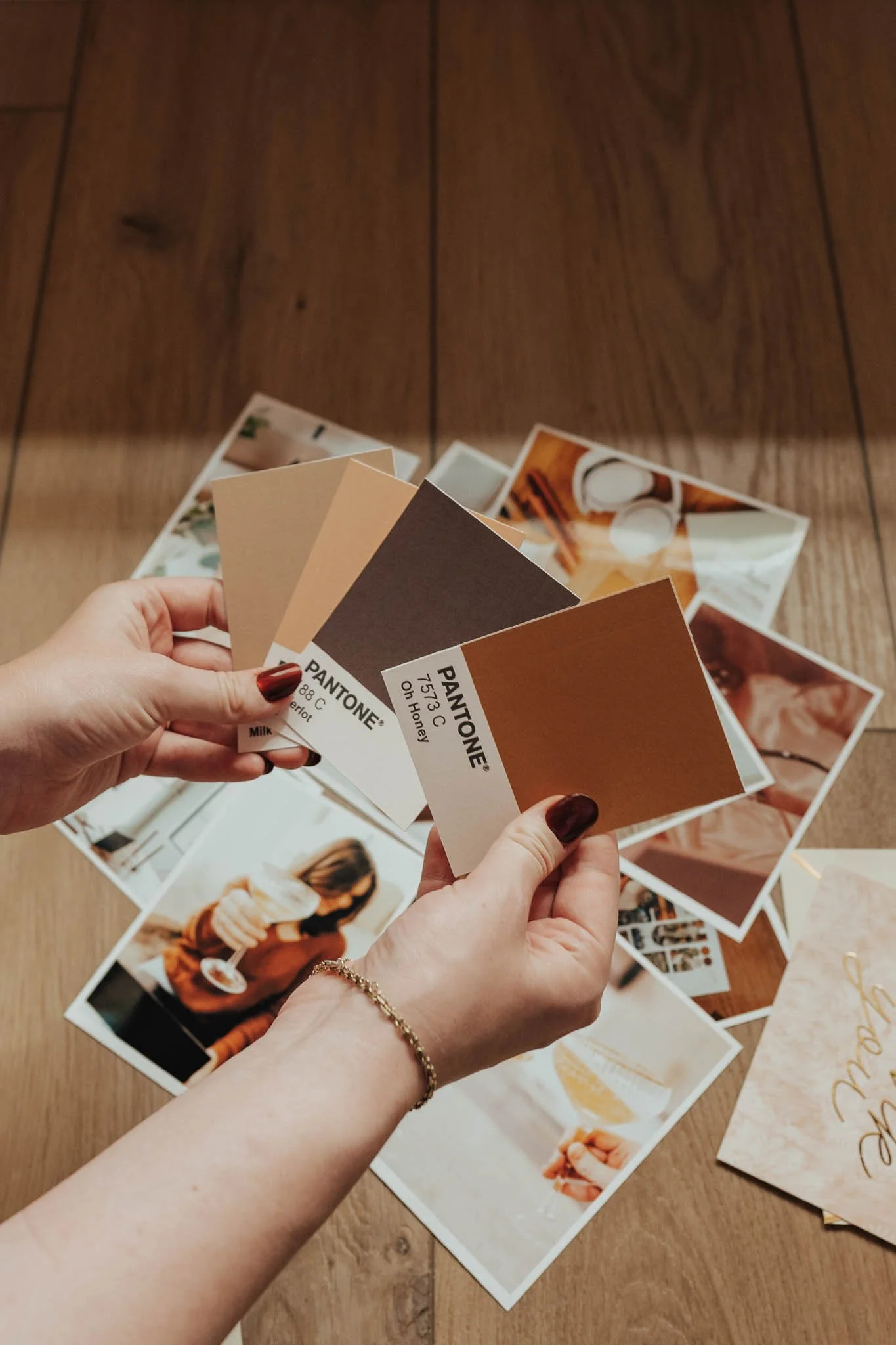 Hands holding Pantone color swatches over a flatlay of brand photos.