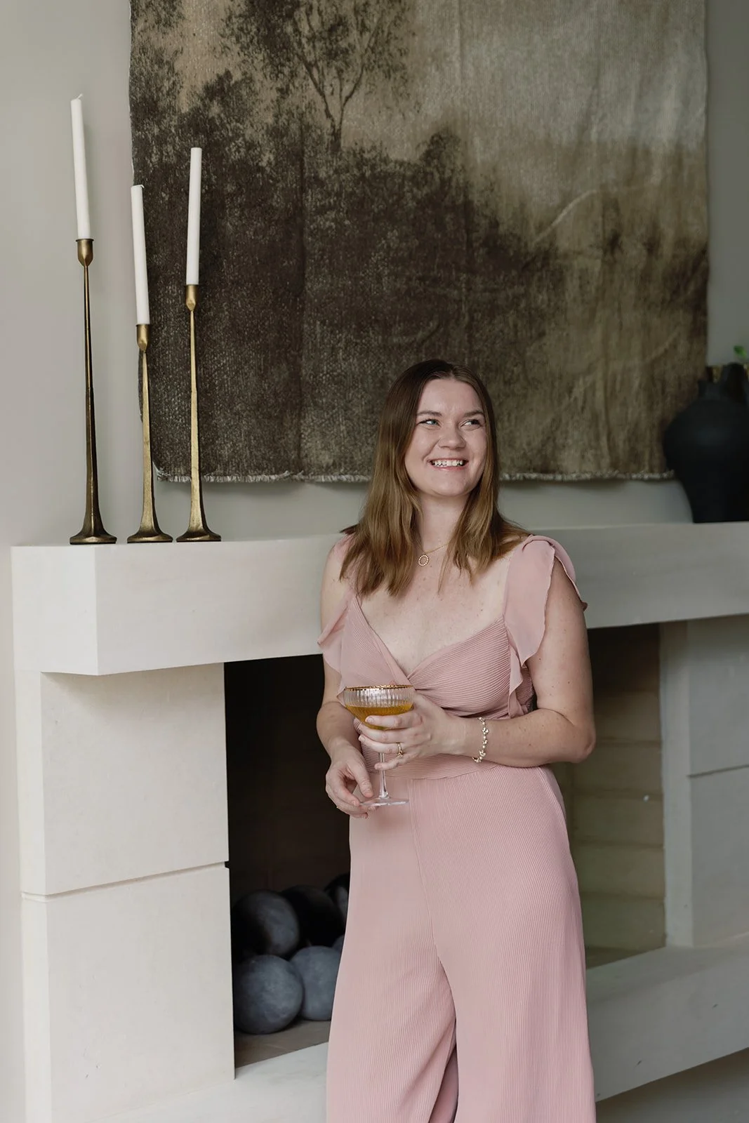 Aliya from Hearthstone Creative standing in front of a hearth, holding a glass of apple cider to celebrate her clients' finished brand identity.