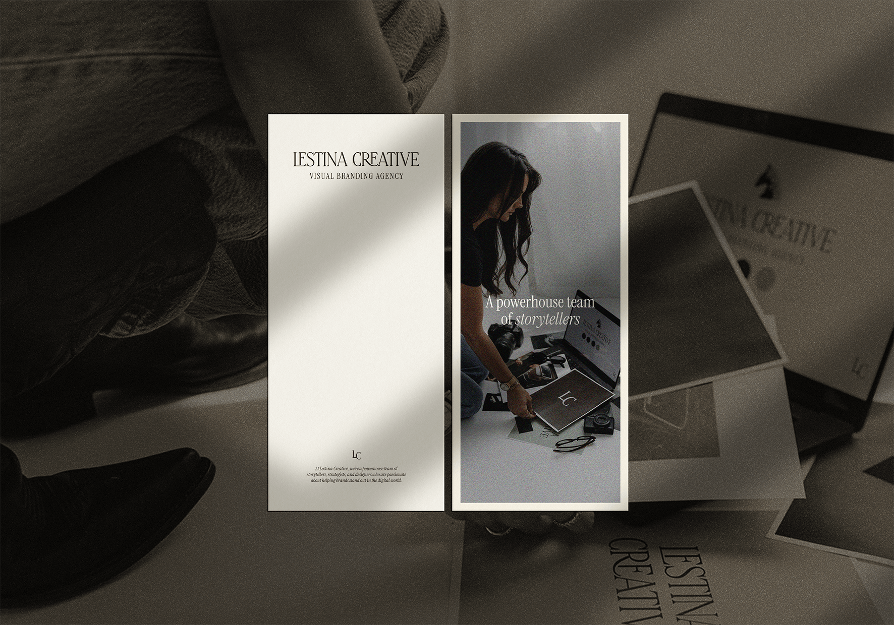Two vertical banners on a desk, one with the text 'LESTINA CREATIVE VISUAL BRANDING AGENCY' and the other showing a woman with long dark hair sitting on the floor with a laptop, camera, and notebooks, with the text 'A powerhouse team of storytellers'.