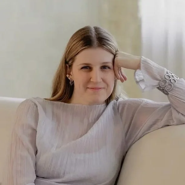 A young woman sits on the couch, propping her head up on her hand.