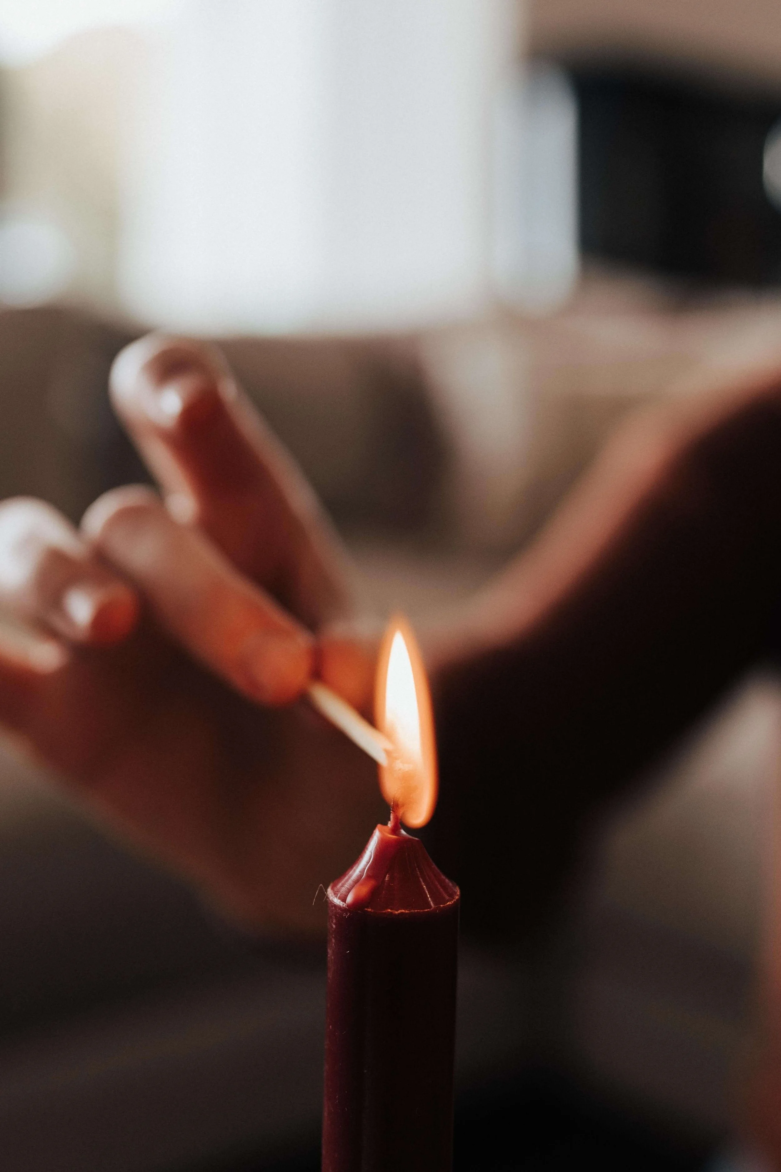 A hand lighting a candle with a lit match.