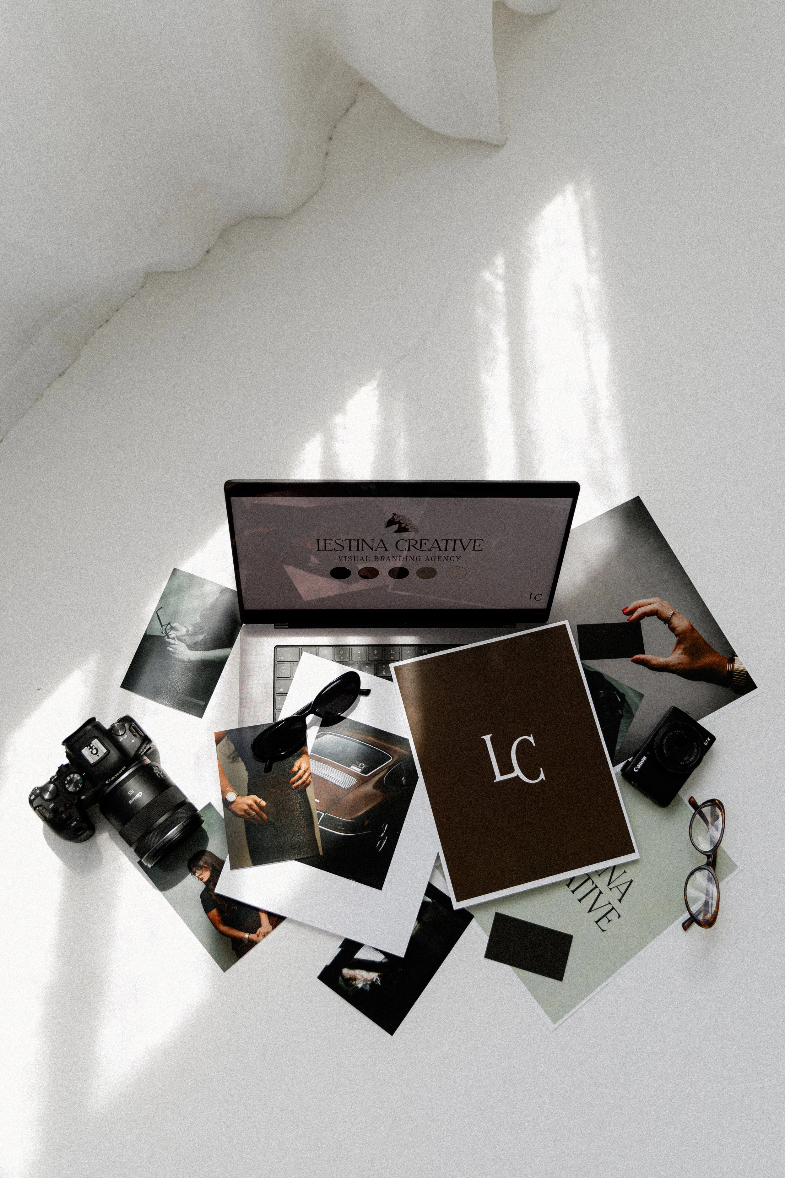 Brand materials for visual branding agency laid out on the floor, featuring a camera, sunglasses, computer, and pages of mood board images.