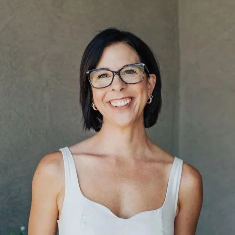 A real estate professional posed for a headshot photo shoot against a gray wall.