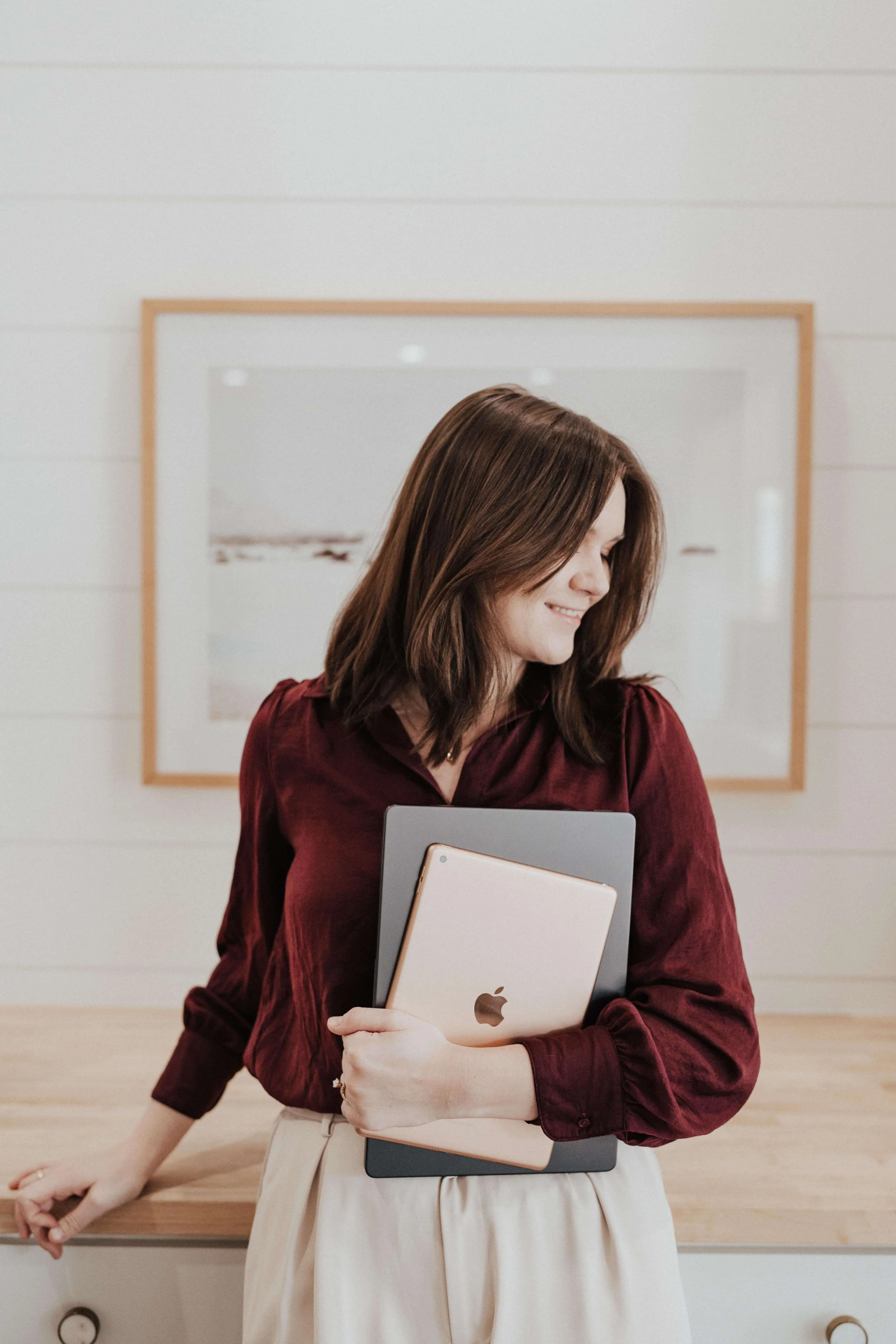A brand designer holding a laptop and an iPad in a well-lit living room environment.