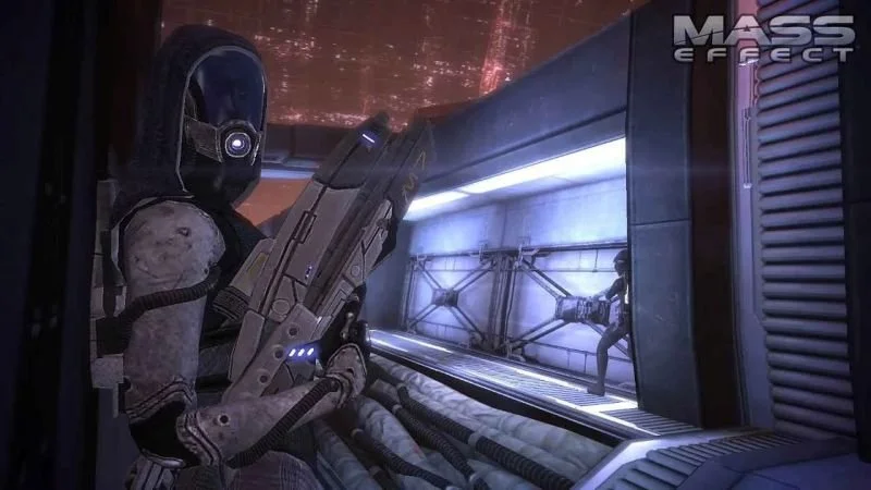 Tali'Zorah nar Rayya from Mass Effect (2007). Screencap features the character at a corner looking over her shoulder toward the viewer with a gun in hand, a potential squad mate behind her further down the course.