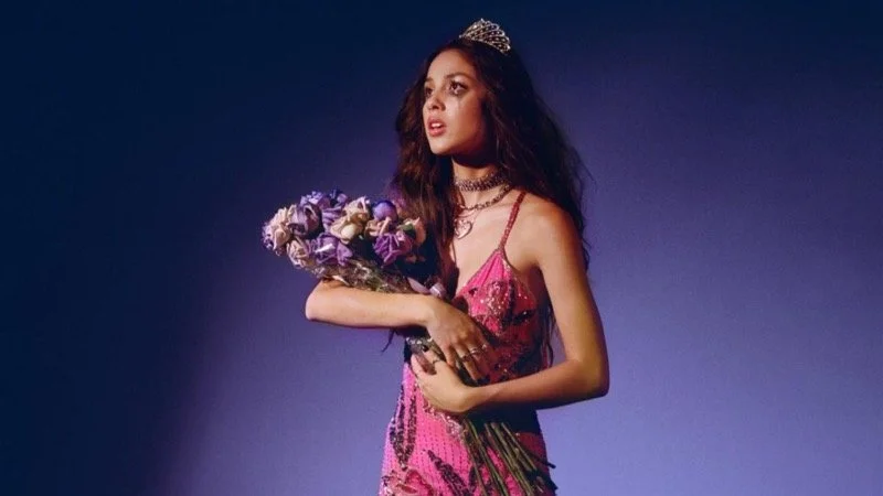 Rodrigo in a prom dress holding a bouquet of flowers   Image Source: mxdwn Music