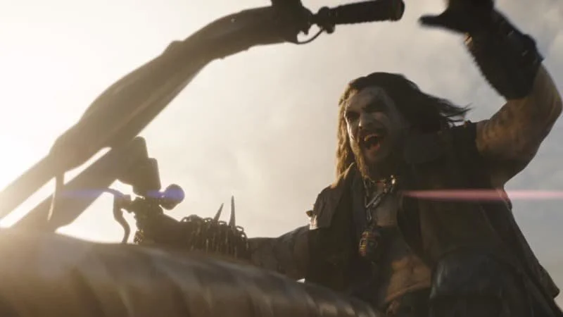 Lobo mounting his motorcycle, the Spacehog, with a grinning laugh. The camera is pointing up towards Lobo from the ground.  Image Source: IMDb