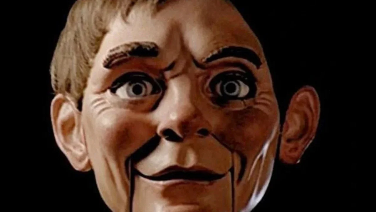 Still of Fats the Ventriloquist dummy from Magic (1978), focusing on the doll’s face. He has thick eyebrows, blue painted eyes, and a crisp, borderline smirking grin