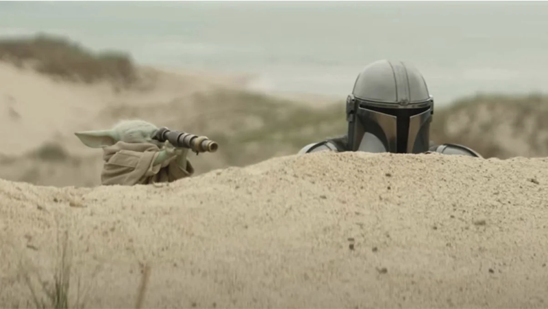 Image depicts Dinn Djarin and Grogu behind a sand dune