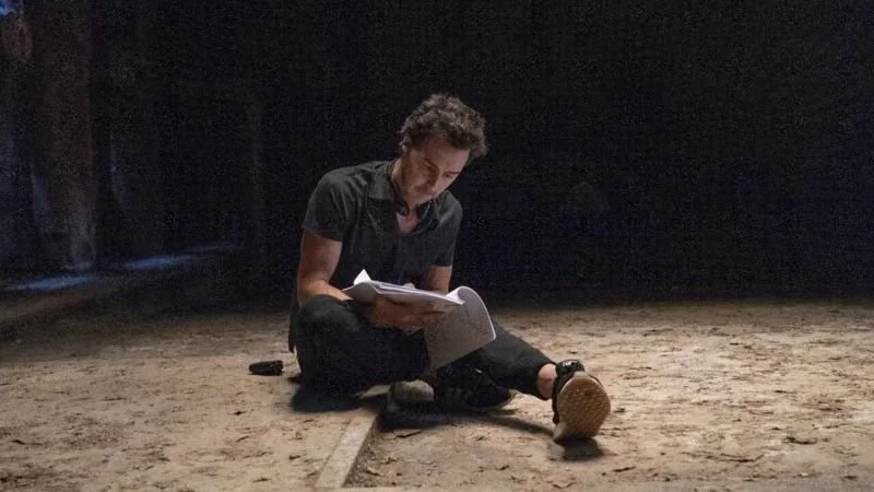 Shawn Levy reading what appears to be a script, sitting in the middle of an intentionally dusty set, one leg crossed and one leg extended.
