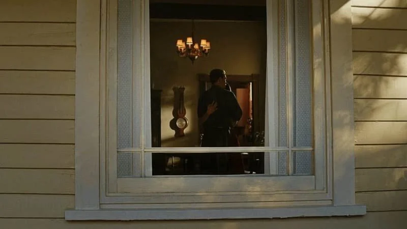 from Avengers: Endgame (2019), Steve and Peggy dancing together in a house under a small chandelier light, the camera giving a view from outside through an off-white framed window surrounded by yellow siding