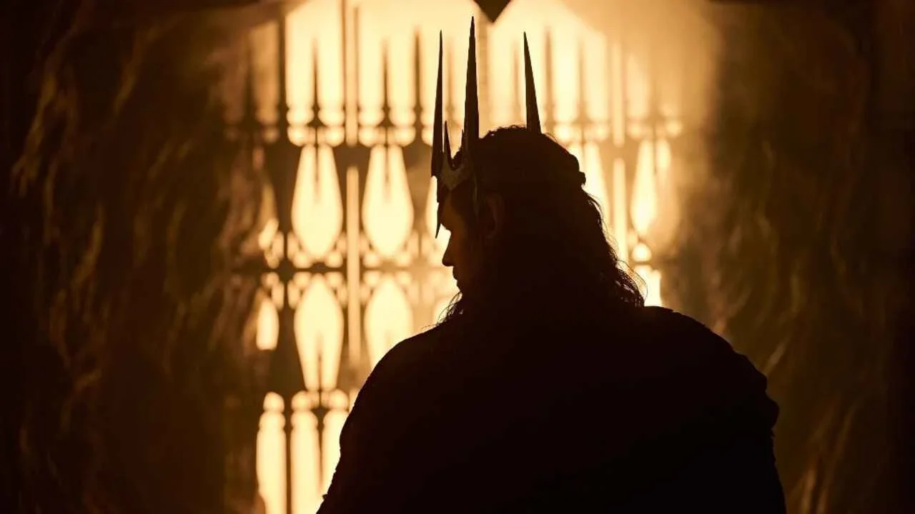 Charlie Vickers as Sauron in a promotional image for the third season of The Rings of Power. Vickers is wearing Morgoth's crown with his back towards the camera, facing what appears to be a forge or fiery hole.