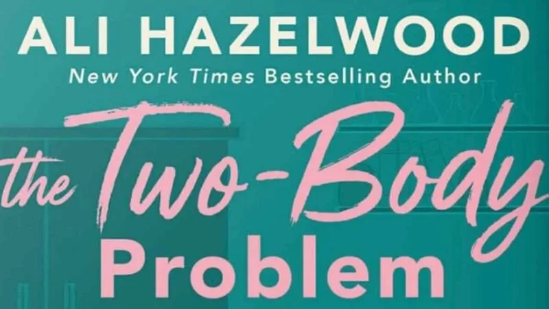 The title from the book cover of The Two-Body Problem, the author's name at the top in pale yellow and the title itself in light pink, all against a seaglass green and teal background.