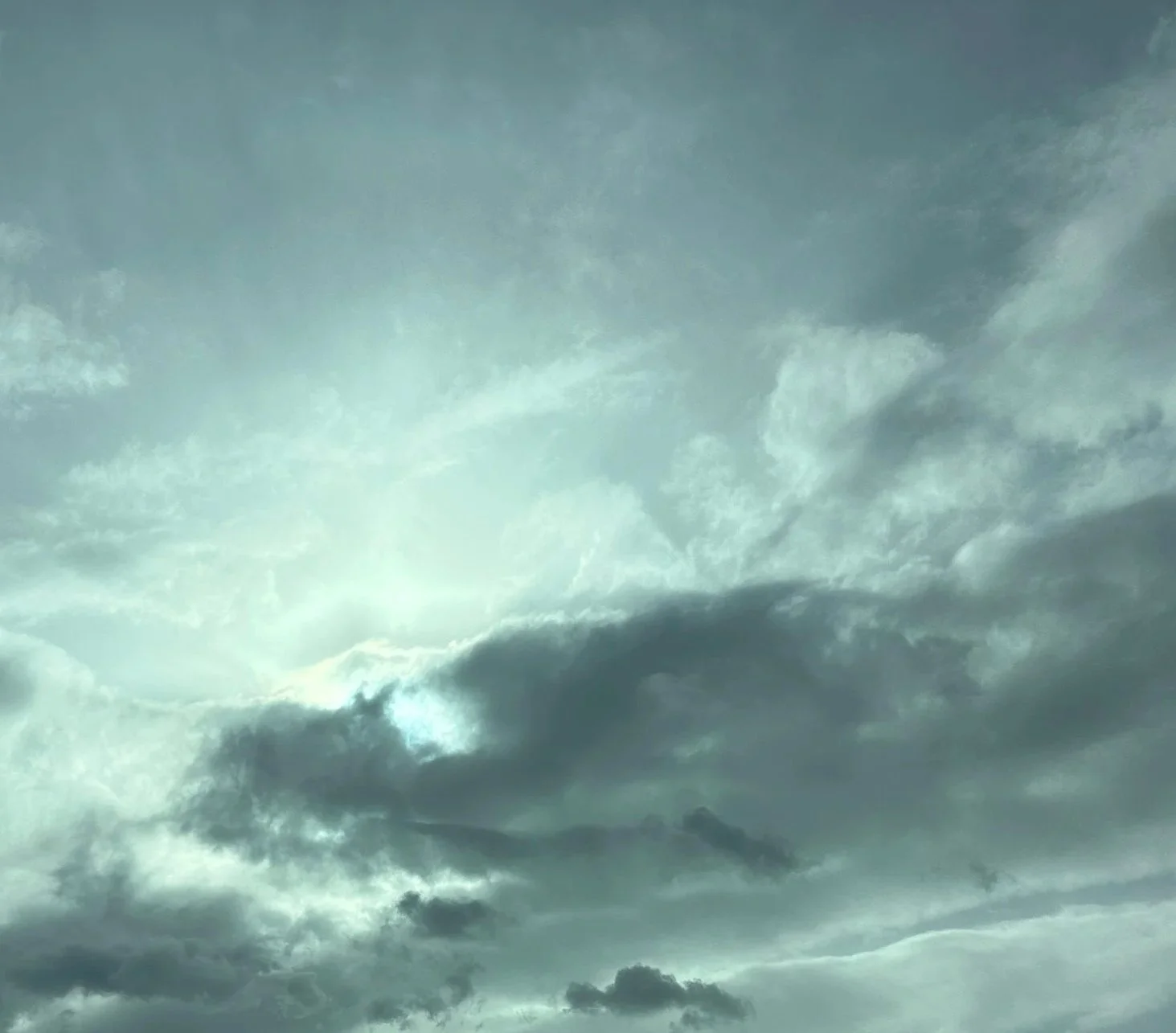 A picture of the sun shining behind layered gray and white clouds