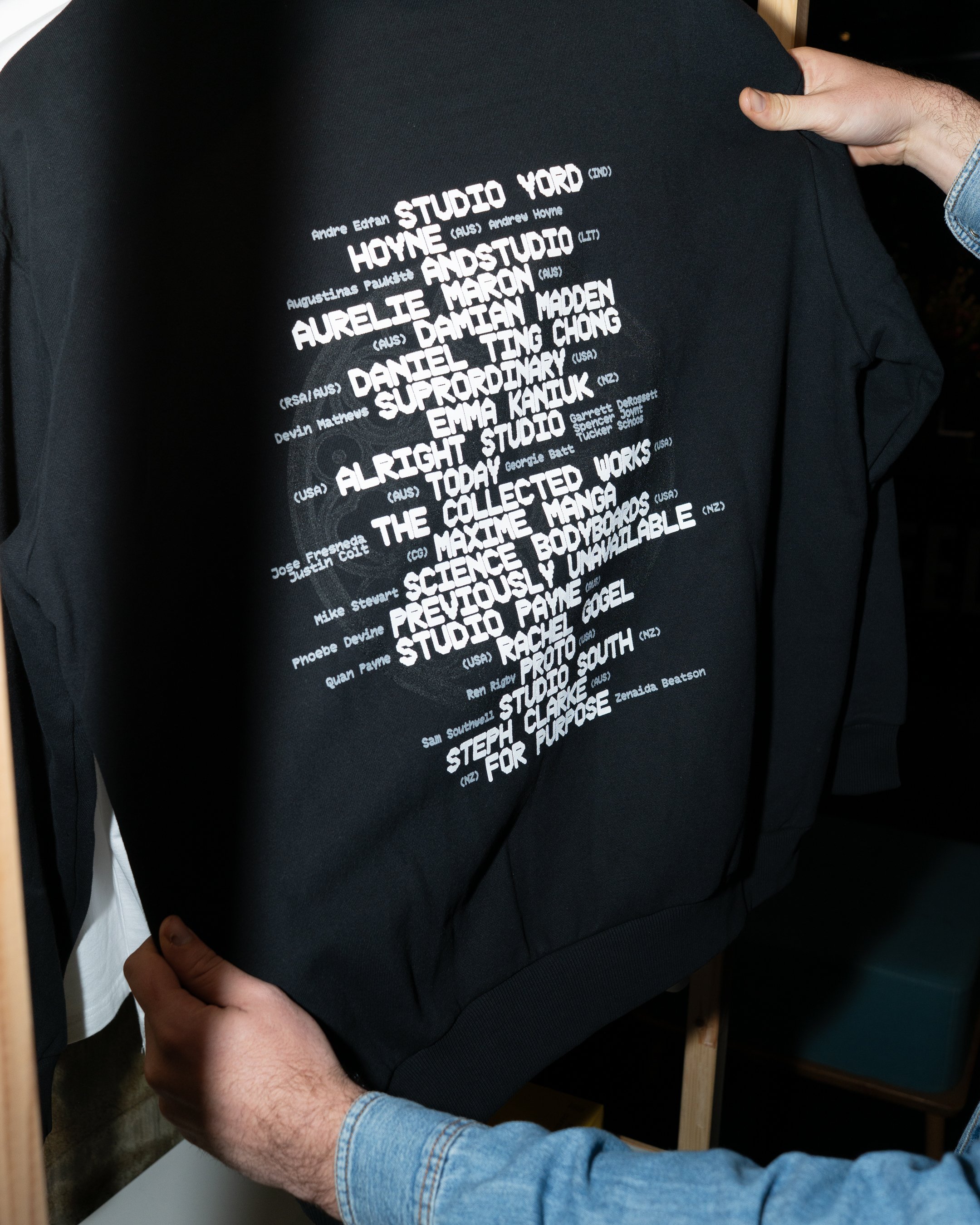 Black sweatshirt with text listing names of individuals associated with Studio Ghibli and Japanese animation, being held by a person in a light blue denim shirt.
